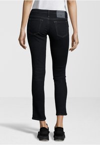 Vaqueros skinny negros de cintura media, con bolsillos traseros y detalles de costura sutiles. Estilizados con zapatillas negras.