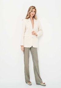 Crème blazer met een enkele knoop, gecombineerd met groen en bordeauxgekleurde gestreepte broek. Kenmerken zijn een notch lapel en een rechte pasvorm.