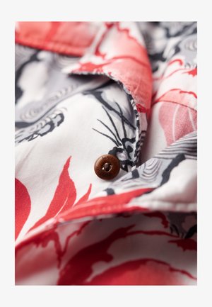Chemise en tissu à motif floral rouge et noir avec un bouton marron portant le texte embossé "SUPERDRY" et un bord texturé.