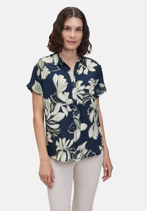 Marineblaue Bluse mit kurzen Ärmeln, die große grüne und weiße Blumenmuster aufweist, eine Knopfleiste hat und einen lockeren Schnitt bietet.