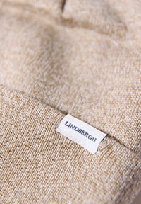 Beige gebreide muts met een gestructureerd patroon; voorzien van een wit label met de merknaam "LINDBERGH" genaaid aan de zijkant.