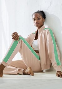 Zweiteiliges Sportoutfit bestehend aus einer hellrosa Zip-Jacke und passenden Hosen. Akzentuiert mit mintgrünen Streifen und weißen Paspelierungen. Glatte Textur.