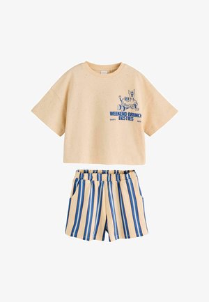 Beiges kurzärmeliges Cropped-Top mit Cartoon-Aufdruck und Schriftzug „Weekend Brunch Besties“, kombiniert mit beigen und blauen, vertikal gestreiften Shorts mit elastischem Bund.
