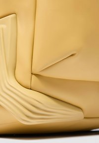 Bolso beige con textura lisa y mate. Presenta un diseño escultórico con superficies curvas y angulares, que resaltan pliegues y costuras distintivos.