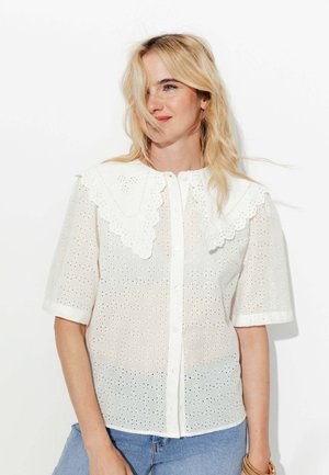 Chemise en coton blanche avec un col en eyelet festonné et des manches courtes, présentant un devant boutonné et un motif perforé texturé.