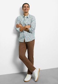 Button-up shirt features a blue floral pattern on a white background. Brown pants and white sneakers complete the outfit.