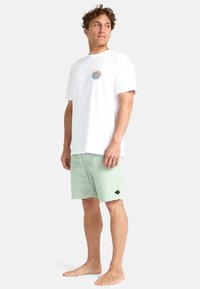 Hvit bomull t-skjorte med et fargerikt grafisk motiv på brystet, kombinert med lysegrønne corduroy-shorts med et svart logo-patch.