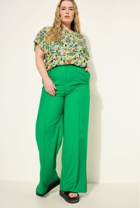 Bloemtop met gele, rode en groene patronen; groene wijde broek; zwarte platform sandalen; gladde texturen en een comfortabele pasvorm.