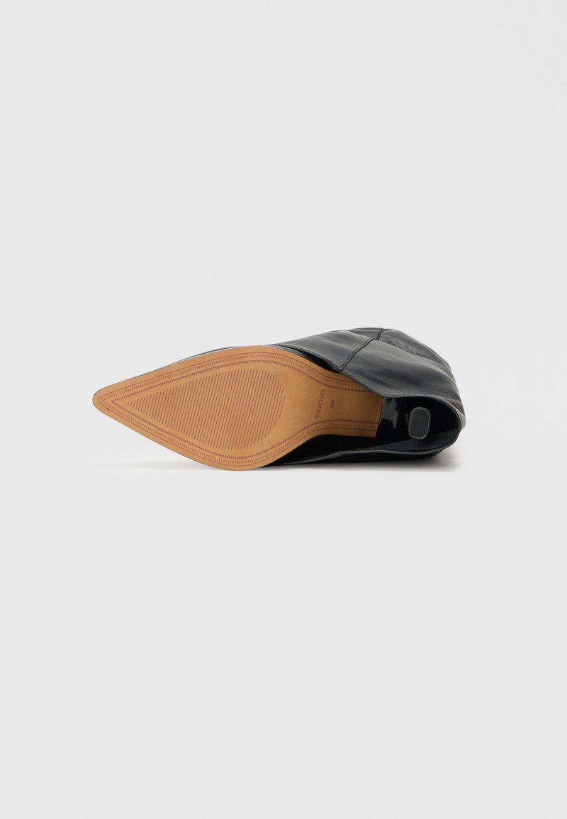 Schwarzer Lederschuh mit spitzer Zehenpartie und einer flachen, strukturierten hellbraunen Gummisohle. Seitendetails umfassen eine glatte Oberfläche mit einer leichten Akzentuierung an der Ferse.