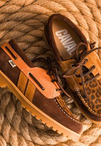 Chaussures décontractées en daim marron et beige avec lacets et détails imprimé léopard, placées sur une surface de corde épaisse enroulée.