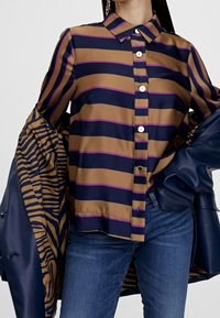 Randig skjorta i brunt, marinblått och lila. Knappt upp-design med krage och en mjuk satinkänsla. Sammanfogas med en blå jacka med randig foder.