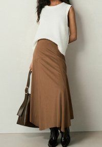 Bílý, bezrukávový, nadýchaný svetr doplněný hnědou, dlouhou, splývavou sukní. Černé, lesklé kotníkové boty a tmavě zelená kabelka na rameno dotvářejí vzhled.