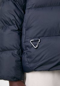 Mörkblå vadderad jacka med quiltad textur, oversized passform och en silverfärgad karbinhake på ärmen.