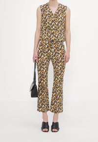 Ensemble deux pièces comprenant un haut sans manches à encolure en V et un pantalon évasé, tous deux ornés d'un motif de feuilles colorées dans des tons de blanc, jaune et brun.