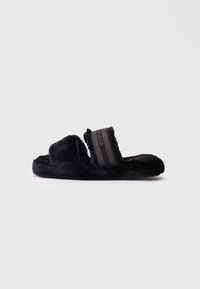 Schwarze Fleece-Pantoletten mit weicher Textur, zwei breiten Riemen und einem kontrastierenden schwarz-gestreiften Design auf dem Riemen. Flache Sohle für Komfort.