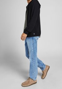 Black zip-up hoodie over a gray layered shirt, paired with light blue jeans and brown suede shoes, featuring textured fabric and a relaxed fit.