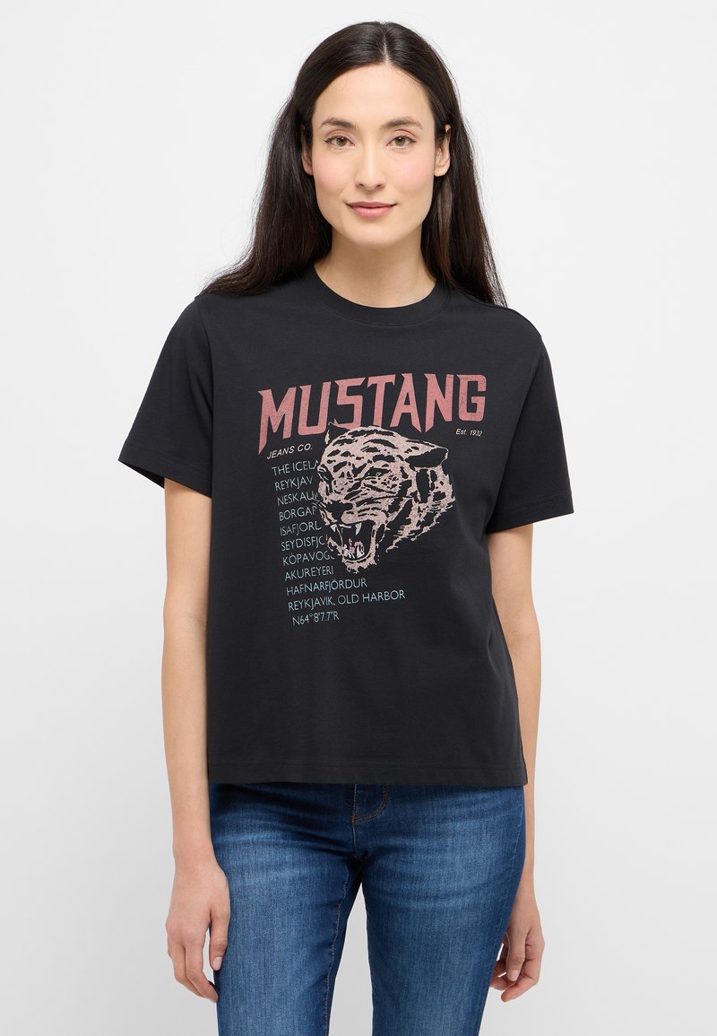 Černé bavlněné tričko s grafikou tygra a textem "MUSTANG" v červené barvě. Krátké rukávy a volný střih, kombinované s modrými džíny.