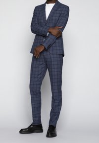Marinblå rutigt kostym med texturerad tyg, bestående av en skräddarsydd kavaj och åtsittande byxor, i kombination med en vit t-shirt och svarta skor.
