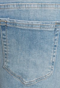 Tecido de jeans azul claro com um bolso traseiro; apresenta um desvanecimento subtil e uma costura ao longo das bordas. Textura suave.