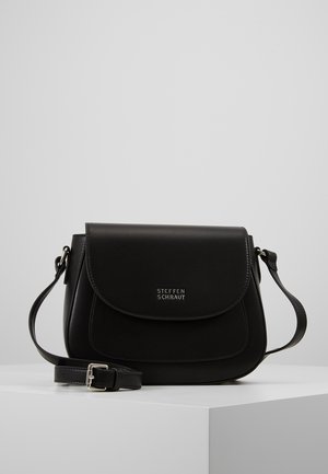 Sac bandoulière en cuir noir avec fermeture à rabat, sangle réglable et logo "Steffen Schraut" sur le devant, présenté sur un socle blanc.