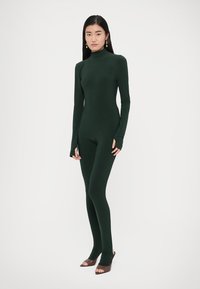 Costum întreg verde închis, cu gât înalt și mâneci lungi. Materialul este neted și mulat, cu găuri pentru degete la capetele mânecilor.