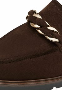 Zapato de ante marrón con un detalle trenzado entrelazado con eslabones metálicos dorados en la parte superior, justo encima de la suela.
