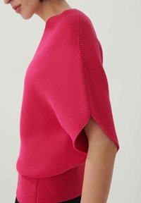 Fuchsiový pletený top s krátkými rukávy, texturovaným vzorem a volným střihem. Má kulatý výstřih a detail vrstveného lemu.