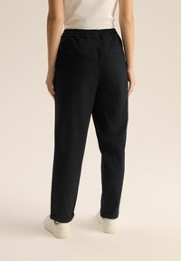 Czarne spodnie o luźnym kroju z elastycznym paskiem w talii, bocznymi i tylnymi kieszeniami oraz mankietami, wykonane z gładkiego, matowego materiału.