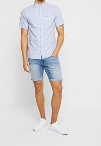 Ljusblå kortärmad skjorta med knappslå och ficka, med ett litet mönster. Bärs med denimshorts och vita sneakers.