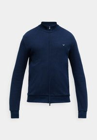 Jachetă de culoare albastru marin, cu fermoar, guler înalt, manșete și tiv cu nervuri, țesătură texturată și un logo brodat pe piept.