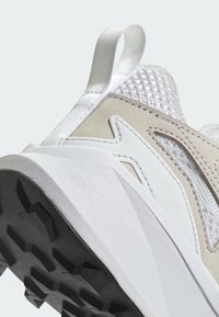 Scarpa sportiva di colore chiaro con una tomaia in rete testurizzata, dettagli in pelle liscia e una suola in gomma nera resistente con un battistrada a motivo.