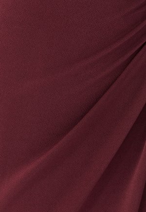 Burgunderfarbener Stoff mit einer glatten, leicht strukturierten Oberfläche, der subtile Drapierungen und geraffte Details aufweist, die Tiefe erzeugen.