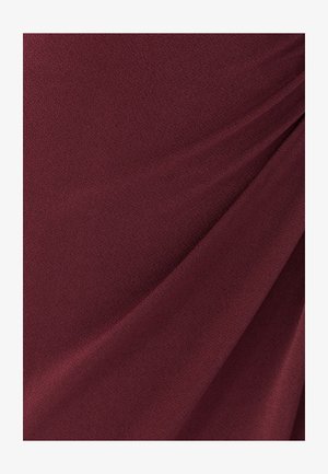 Bordeaux stof met een glad, lichtjes gestructureerd oppervlak, voorzien van subtiele plooien en geplooide details die diepte creëren.