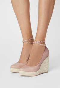 Bottines à talons compensés en simili cuir rose avec un talon en jute tissé, comportant une double sangle de cheville avec des accents cloutés et un bout rond.