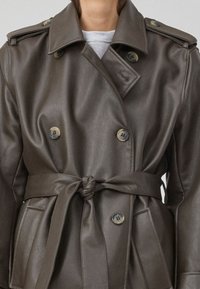Brun skinn dobbeltspent trenchcoat med belte i livet, skulderepauletter, store knapper og sidelommer. Glatt tekstur.