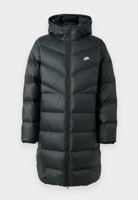 Chaqueta de plumas negra con capucha, con un patrón de acolchado en forma de chevrón, cierre frontal de cremallera completa y un pequeño logo blanco en el pecho.
