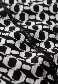 Textil en blanco y negro con un diseño estampado de formas irregulares; superficie texturizada con un ligero acanalado y costuras visibles que acentúan el diseño.