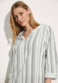 Blusa leggera a righe in azzurro pallido e bianco con linee verticali nere, scollo a V e maniche a tre quarti, caratterizzata da una vestibilità morbida.