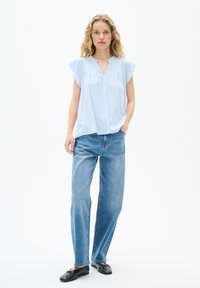 Blusa azzurra a maniche corte con scollo a V e chiusura a bottoni frontali, abbinata a jeans blu a vita alta e fit morbido e ballerine nere.