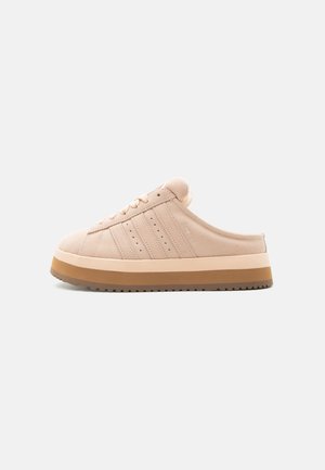 Beżowy sneaker typu slip-on z sznurowanym przodem, cholewka z zamszu, przeszywane paski i gruba dwukolorowa brązowa podeszwa na neutralnym tle.