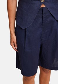 Marineblå linshorts med en relaxed fit, med frontfolder og sidelommer, parret med en matchende skræddersyet blazer.