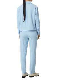 Lichtblauw gecoördineerde outfit met een langermige blouse met kraag en bijpassende broek. De stof heeft een soepele textuur en bevat knoopaccenten.