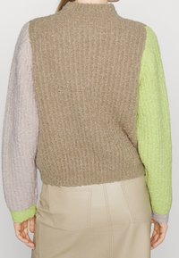 Pull en maille avec texture côtelée, dos beige, manches violet clair et vert citron, col ajusté et couleurs contrastées.
