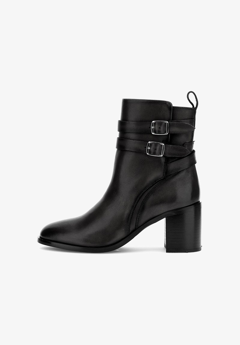 Musta nahkasaapas nilkkapituisella, jossa on paksu korko, kaksi hopeista solkiriipusta yläosassa ja vetotappi takana.