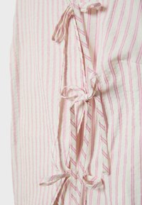 Gros plan sur un tissu crème à fines rayures verticales roses, avec plusieurs nœuds attachés faits du même tissu rayé.