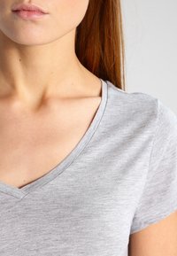 T-shirt grigio a V con maniche corte, realizzato in tessuto morbido. Il collo presenta una finitura pulita e una sottile texture.