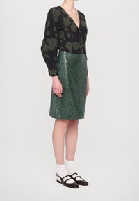 Černý top s dlouhým rukávem a zeleným květinovým vzorem; zelená lesklá kožená tužková sukně; hnědé boty Mary Jane s bílými ponožkami.