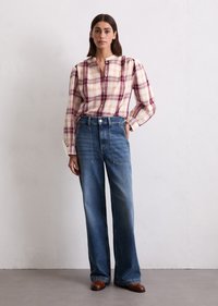 Chemise à manches longues, à carreaux crème, bordeaux et jaune avec une patte de boutonnage, associée à un jean en denim bleu taille haute et à jambes larges.