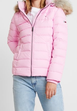 Pink puffer jacket with a fur-lined hood, quilted design, front zipper, and side pockets. Styled with light blue jeans.