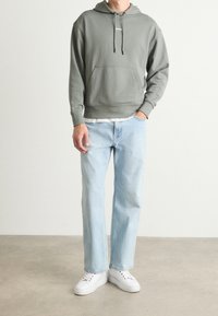 Felpa verde chiaro con tasca frontale e cordini; abbinata a jeans dritti blu chiaro e sneakers bianche. Design semplice.